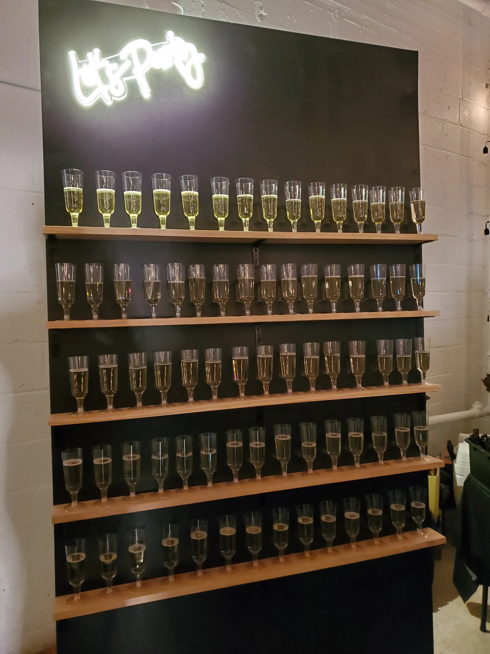 Rows of champagne flutes on a dark shelf beneath a neon sign